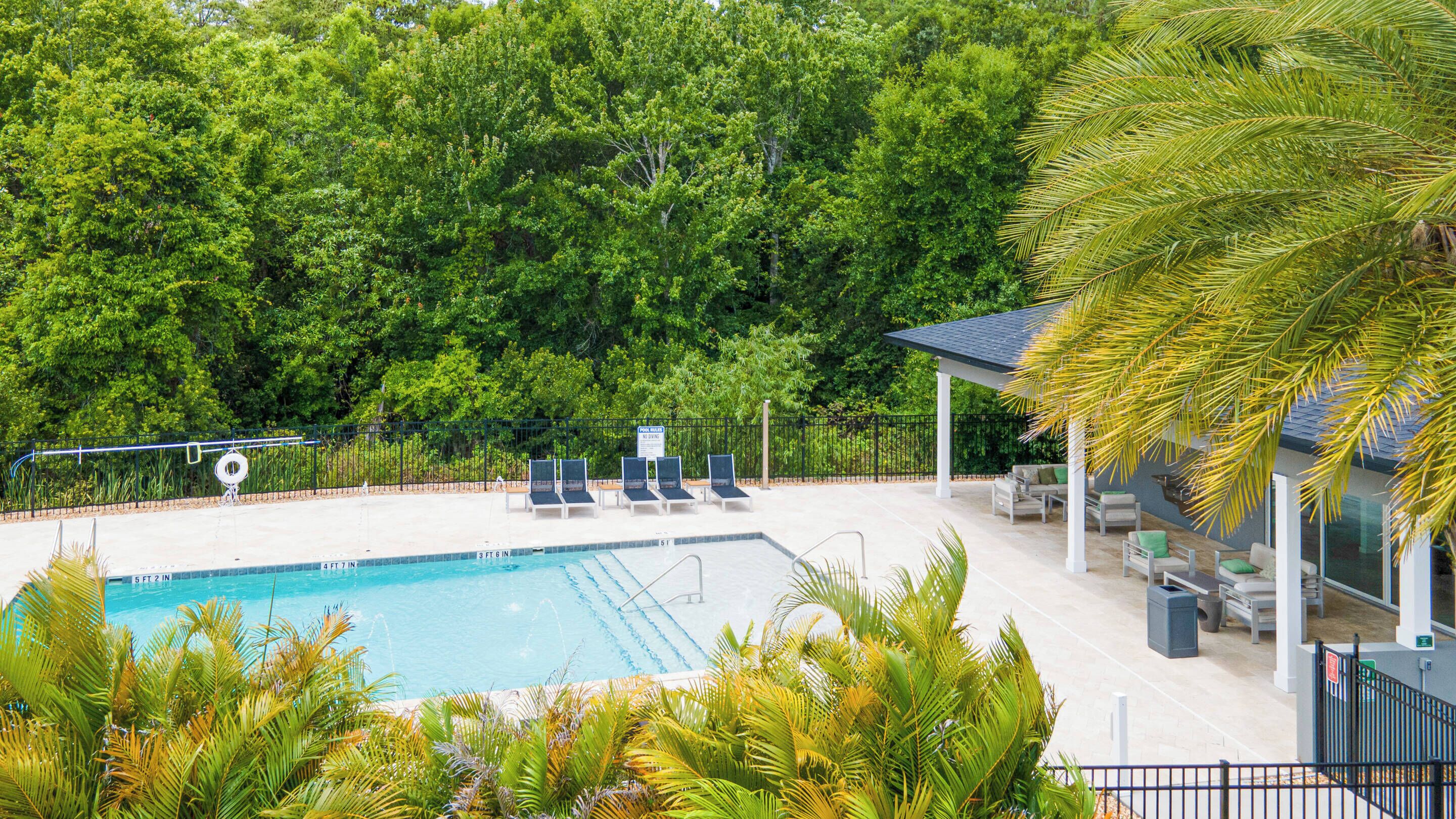 A swimming pool with lounge chairs and a covered seating area, surrounded by lush greenery.