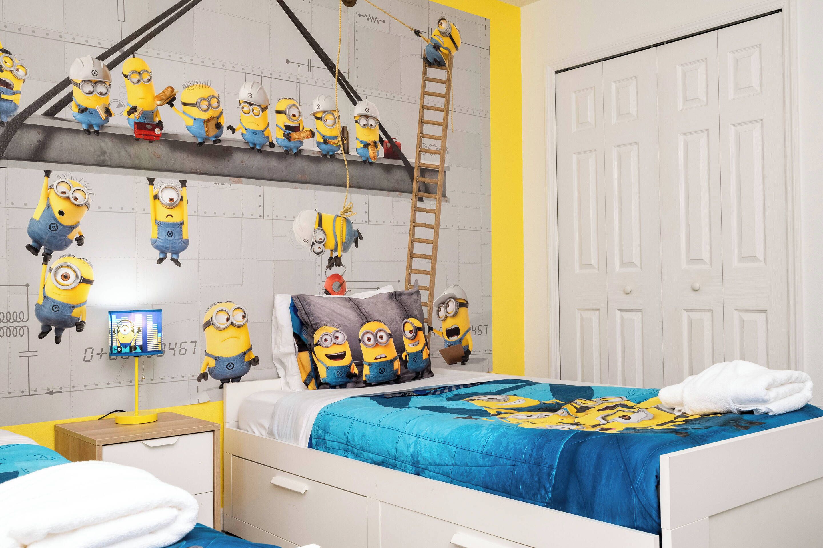 Et soveværelse med seng, skrivebord og væg dekoreret med Minion-motiver.