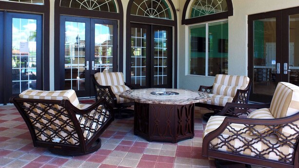 A patio area with a round table and four cushioned chairs, large arched doors, and a tiled floor. - Lake View Home With Private Pool at Bella Vida 91 (Kissimmee)