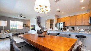 A modern kitchen with wooden cabinets, a large island, and a dining area with a wooden table and chairs. - Lake View Home With Private Pool at Bella Vida 91 (Kissimmee)
