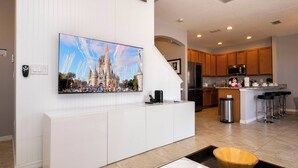 A modern kitchen with white cabinetry, a large flat-screen TV mounted on the wall, and a wooden bowl on the counter. - Lake View Home With Private Pool at Bella Vida 91 (Kissimmee)