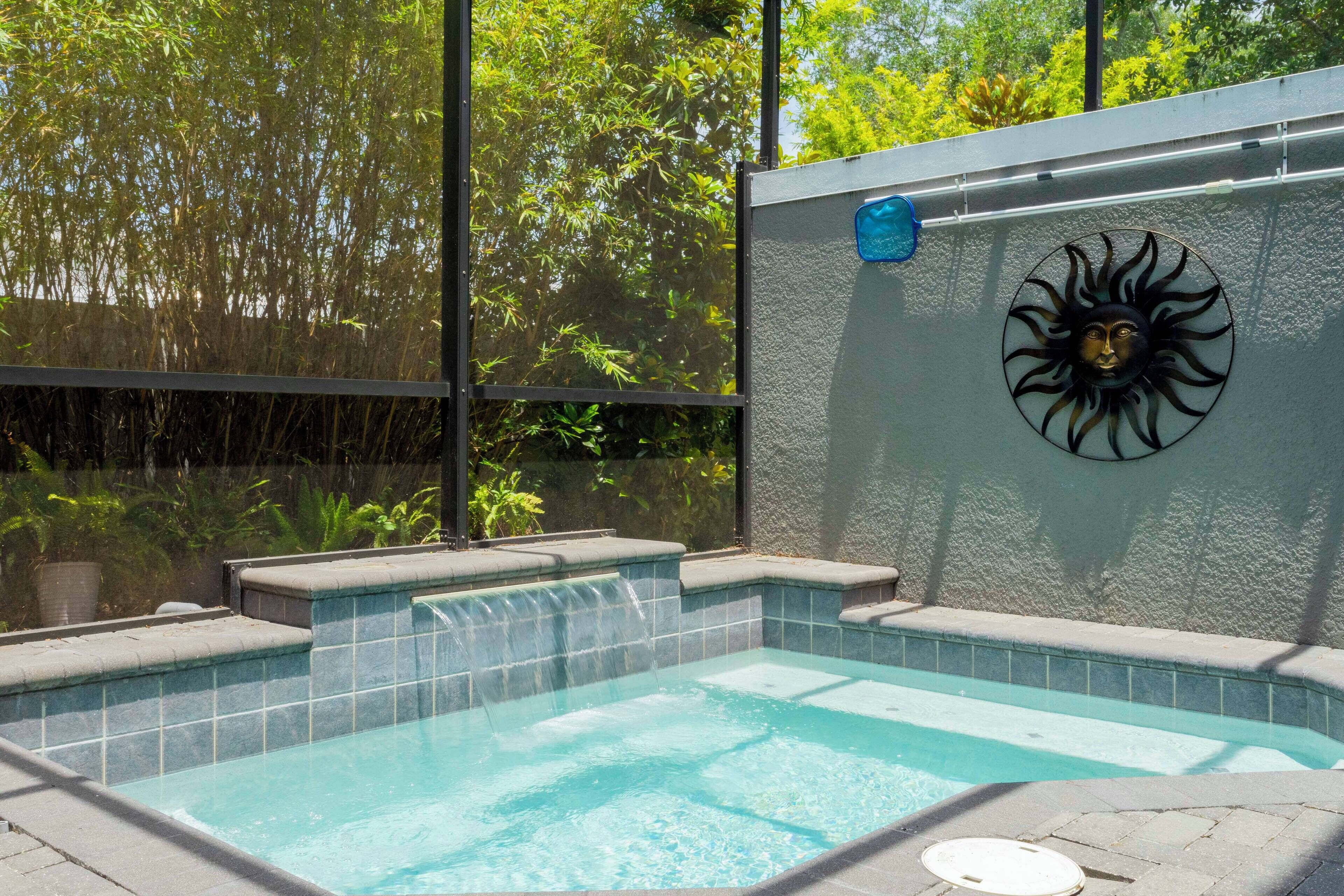 Piscina retangular com cascata, rodeada por um deck de pedra e um muro com motivo solar decorativo.