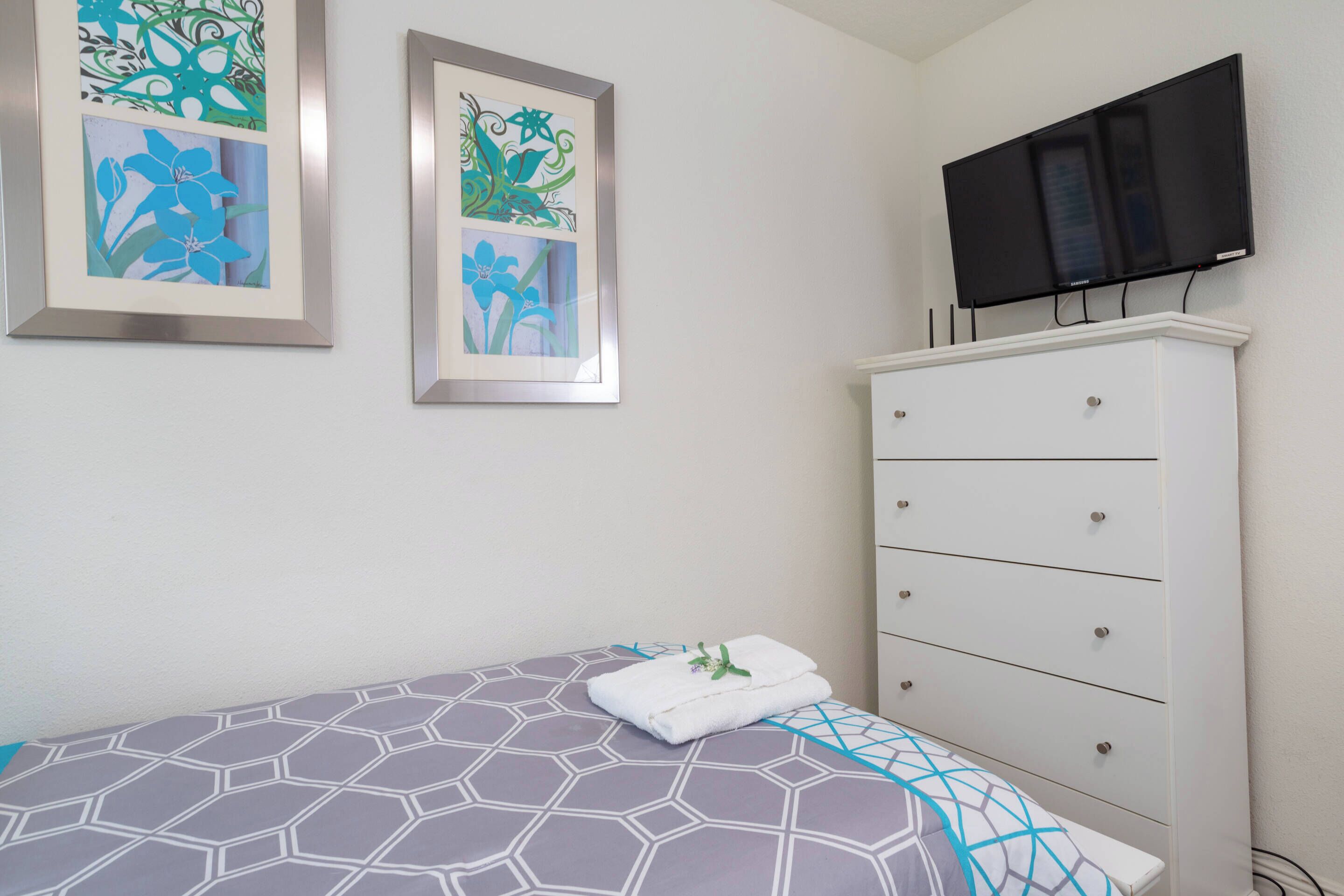 A bedroom with a bed, a dresser, and a flat-screen TV mounted above it.