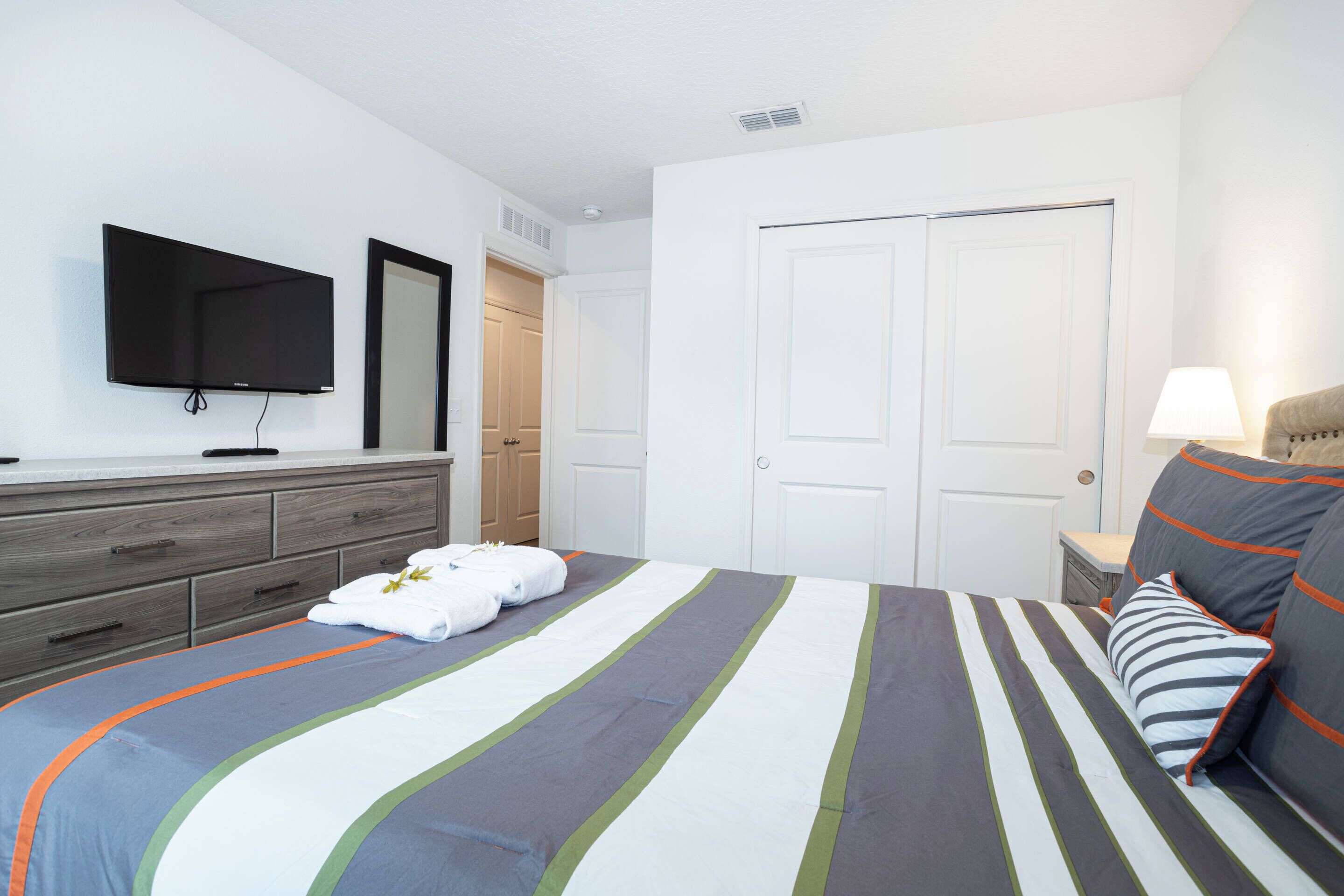 A neatly arranged hotel room with a bed, a TV mounted on the wall, a dresser, and a door.