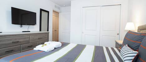 A neatly arranged hotel room with a bed, a TV mounted on the wall, a dresser, and a door.