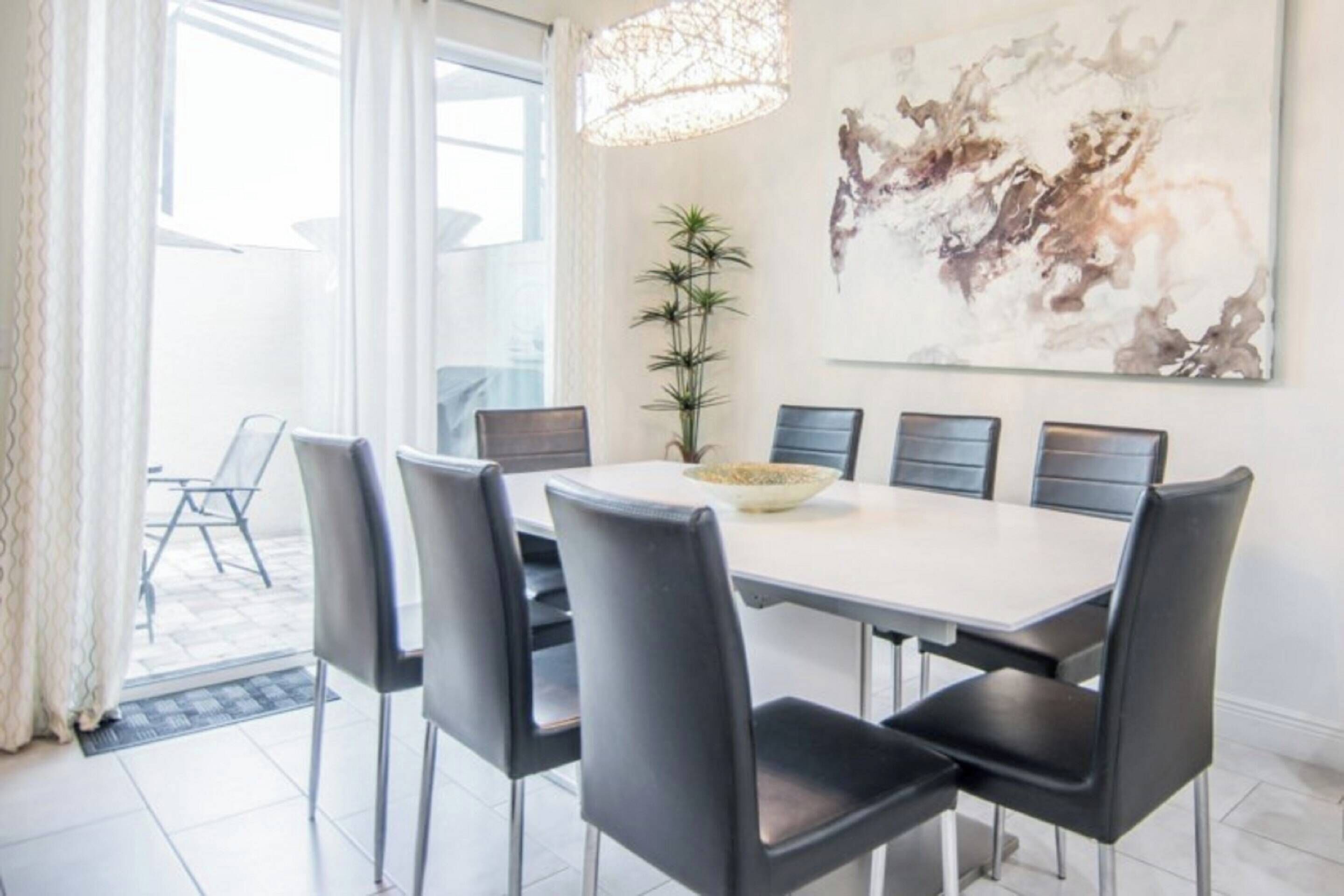 A modern dining area with a white table, black chairs, and a large abstract painting on the wall.