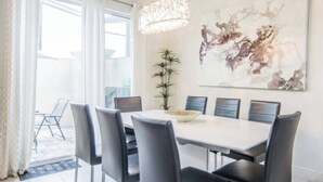 A modern dining area with a white table, black chairs, and a large abstract painting on the wall.