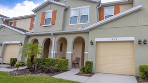 A modern two-story residential building with a beige facade, arched entryways, and a garage numbered 3213.