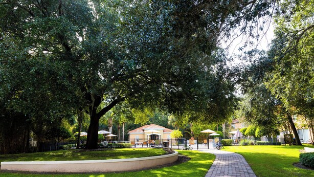A paved pathway leading to a building with a red roof, surrounded by lush greenery and trees.