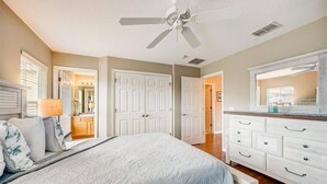 A bedroom with a bed, a ceiling fan, white doors, a dresser, and a mirror.
