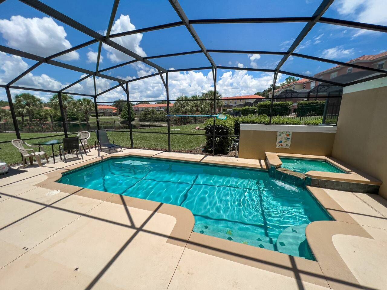 A swimming pool with a glass enclosure, surrounded by a patio area with chairs and a table.