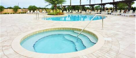 A swimming pool with a hot tub, surrounded by lounge chairs and palm trees.
