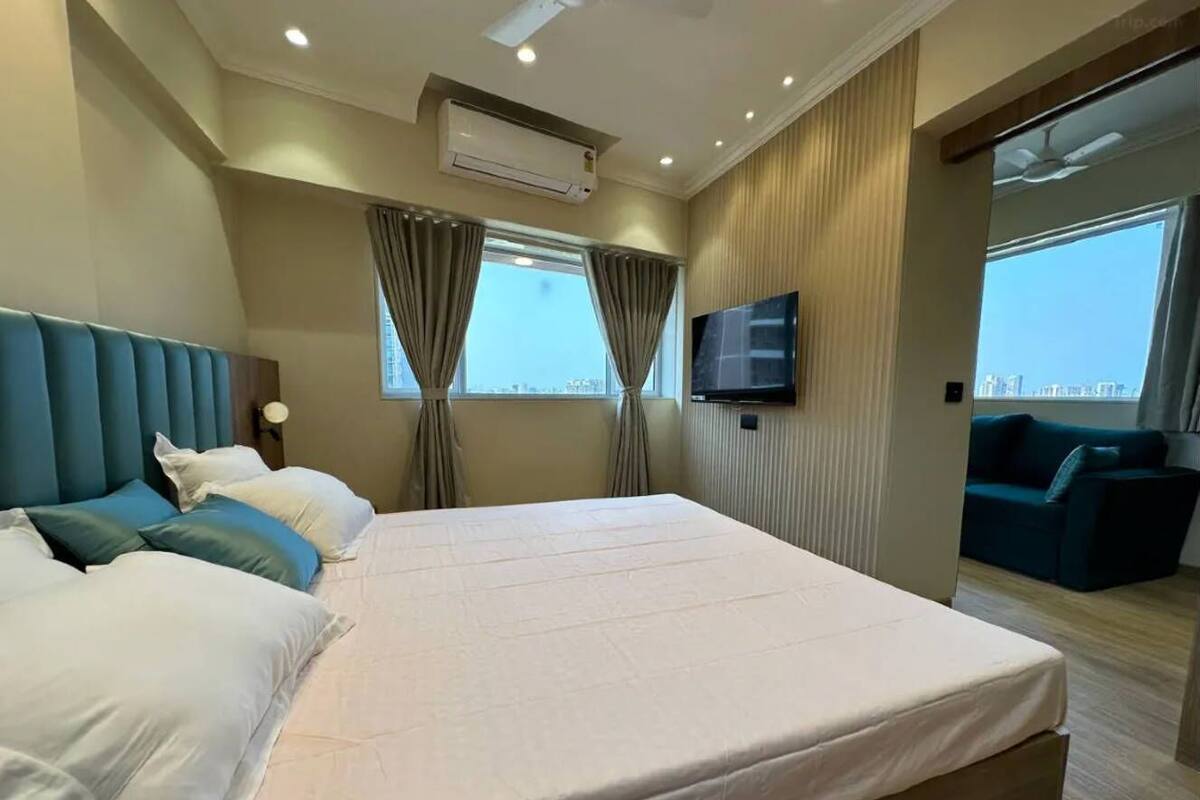 A hotel room with a large bed, a TV, a sofa, and a view of the city.
