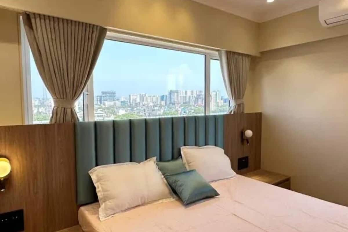 A hotel room with a large bed, a headboard, and a view of a cityscape through a window.