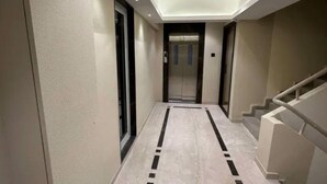 A hallway with a marble floor, a glass door, and a staircase with a handrail. - Rudraya Homes (Mumbai)