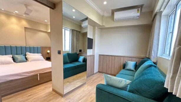 A modern hotel room with a bed, a green sofa, and a large window. - Rudraya Homes (Mumbai)