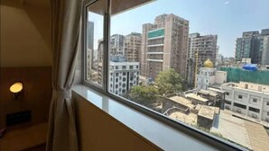A room with a large window overlooking a cityscape with multiple high-rise buildings. - Rudraya Homes (Mumbai)