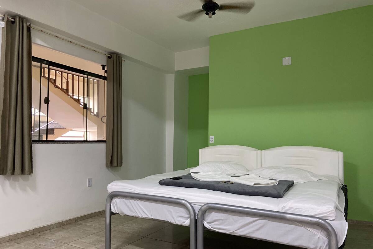 A room with a bed, a ceiling fan, a window with curtains, and a green wall.