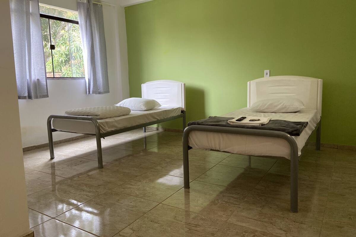 A room with two single beds, a window with curtains, and a green wall.