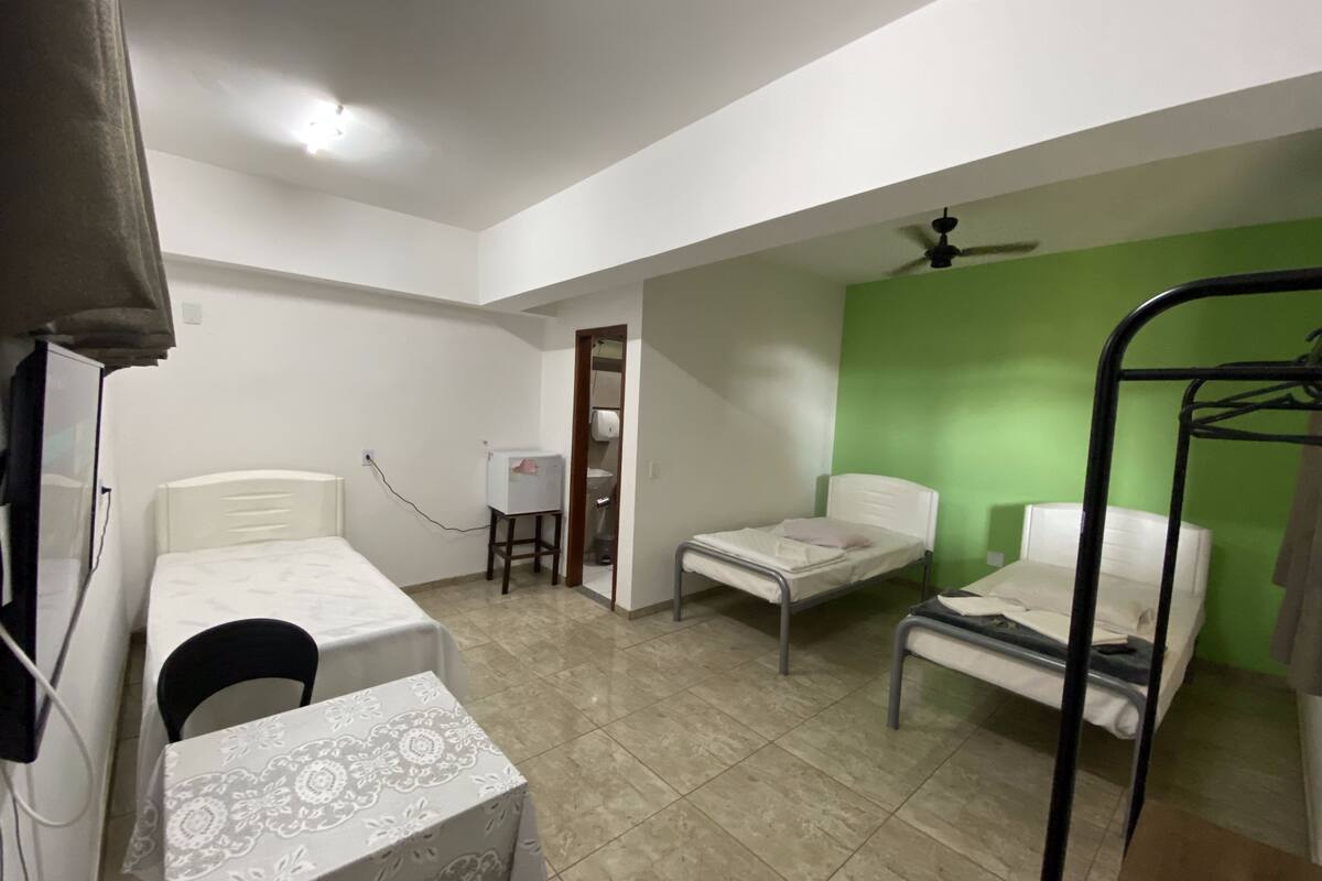 A dormitory room with two single beds, a desk, a chair, and a small table.