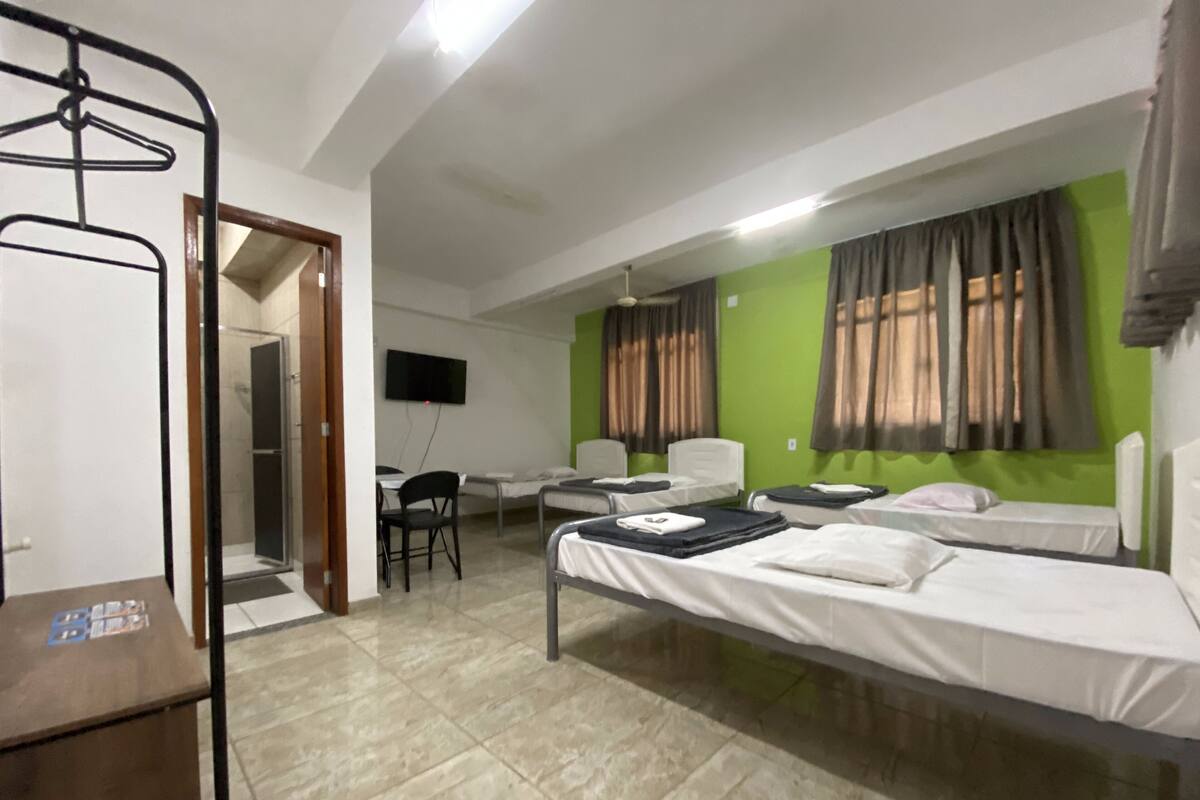 A hotel room with two single beds, a desk with a chair, a TV mounted on the wall, and a bathroom with a shower and toilet.