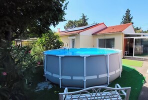 Une piscine hors sol, équipée d’une échelle, entourée d’une pelouse bien entretenue et d’une maison avec un toit rouge.