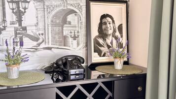 A desk with a vintage rotary phone, a framed photograph, and two potted lavender plants on a textured mat.