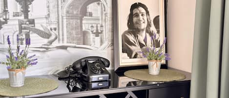 A desk with a vintage rotary phone, a framed photograph, and two potted lavender plants on a textured mat.