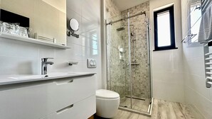 A modern bathroom with a glass-enclosed shower, a toilet, and a vanity with a mirror and shelves. - Hotel Del Medio (Sutomore)