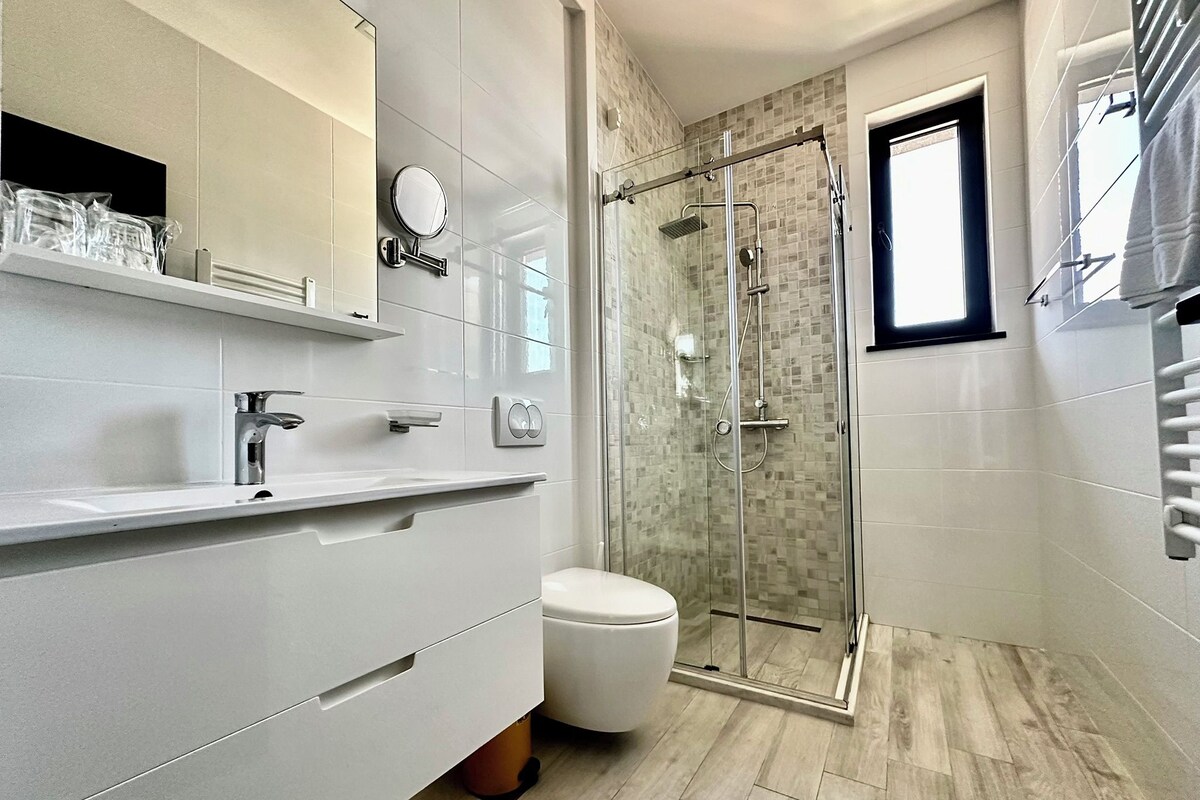 A modern bathroom with a glass-enclosed shower, a toilet, and a vanity with a mirror and shelves.
