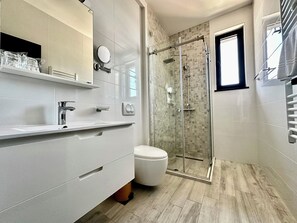 A modern bathroom with a glass-enclosed shower, a toilet, and a vanity with a mirror and shelves. - Hotel Del Medio (Sutomore)