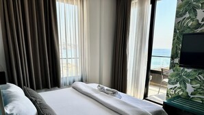A hotel room with a bed, curtains, a TV, and a view of the sea. - Hotel Del Medio (Sutomore)