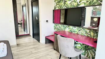 A modern room with a wooden floor, a desk with a pink top, a chair, a large mirror, and a TV.