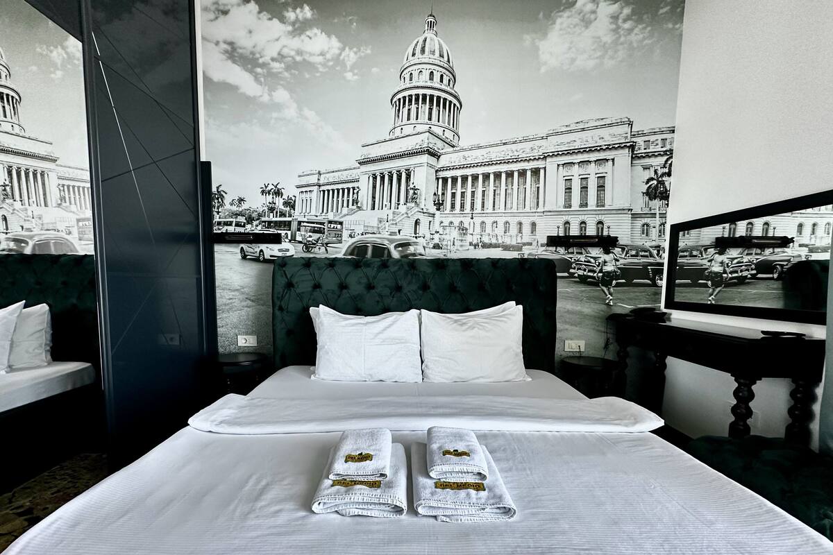 Habitación de hotel con una cama grande, dos almohadas y dos toallas con logotipos del hotel. Un ventanal ofrece vistas de un edificio histórico y una escena callejera.