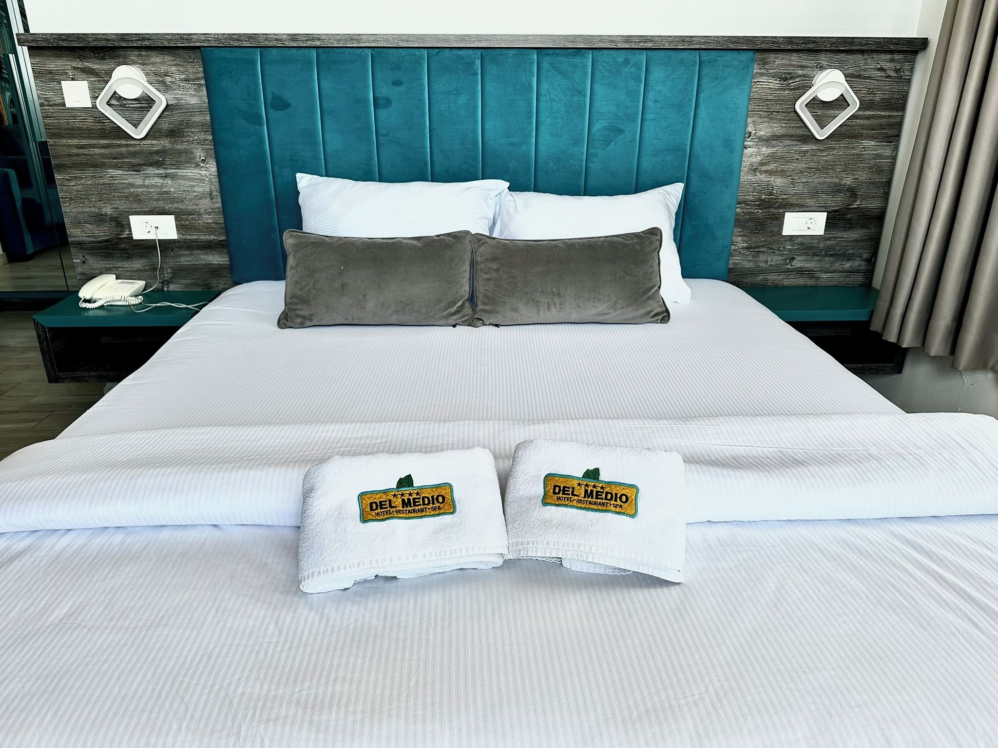 A neatly made bed with white linens, two pillows, and two towels with a hotel logo.