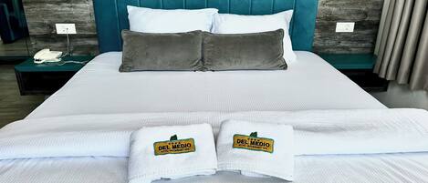 A neatly made bed with white linens, two pillows, and two towels with a hotel logo.