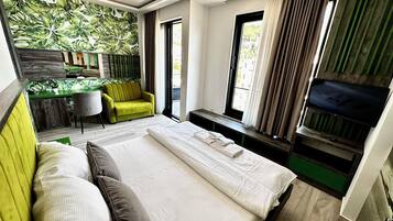 A modern hotel room with a large bed, a desk with a chair, a sofa, and a TV mounted on the wall.