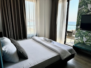 A hotel room with a bed, curtains, a TV, and a view of the sea. - Hotel Del Medio (Sutomore)