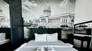 A hotel room with a large bed, two pillows, and two towels with hotel logos. A large window offers a view of a historic building and a street scene. - Hotel Del Medio (Sutomore)