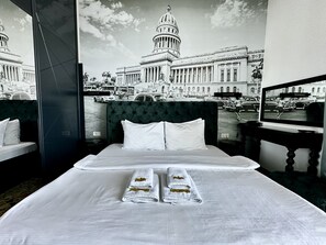 A hotel room with a large bed, two pillows, and two towels with hotel logos. A large window offers a view of a historic building and a street scene. - Hotel Del Medio (Sutomore)