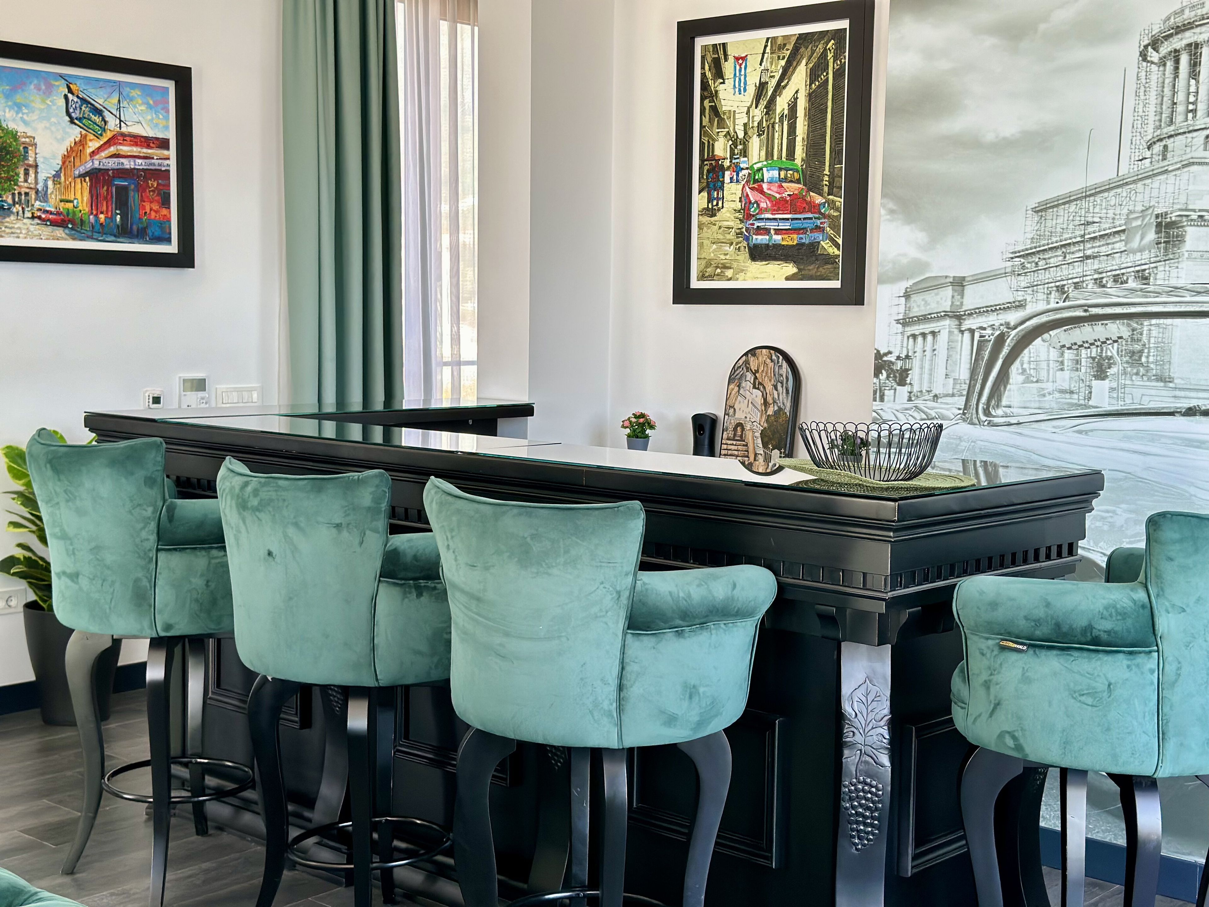 Een moderne bar met een lange toonbank, vier barstoelen en ingelijste kunstwerken aan de muur.