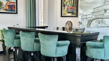 Een moderne bar met een lange toonbank, vier barstoelen en ingelijste kunstwerken aan de muur.