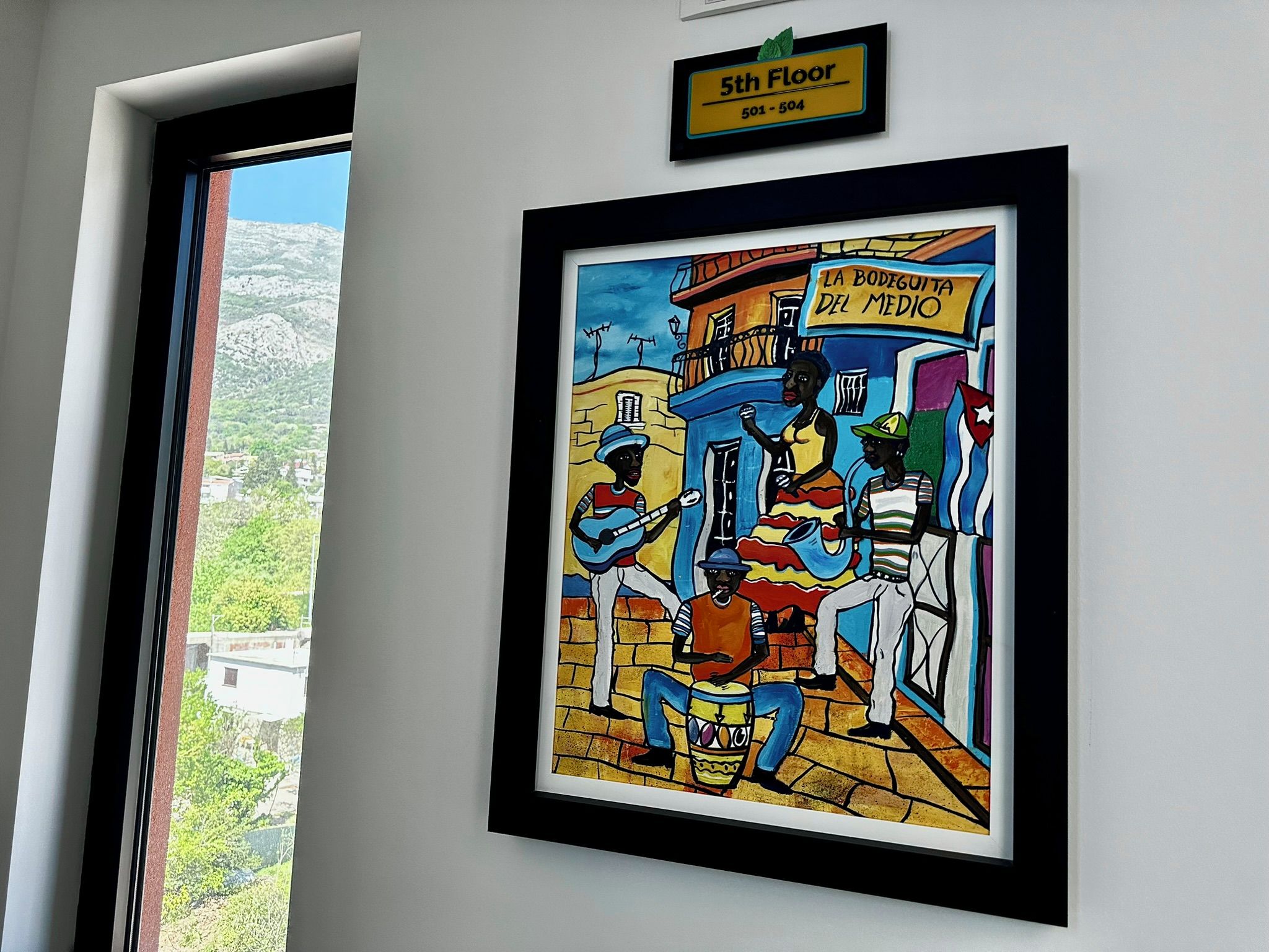 A framed artwork depicting a street scene with musicians and a sign reading "LA BODEGUITA DEL MEDIO" on the 5th floor.