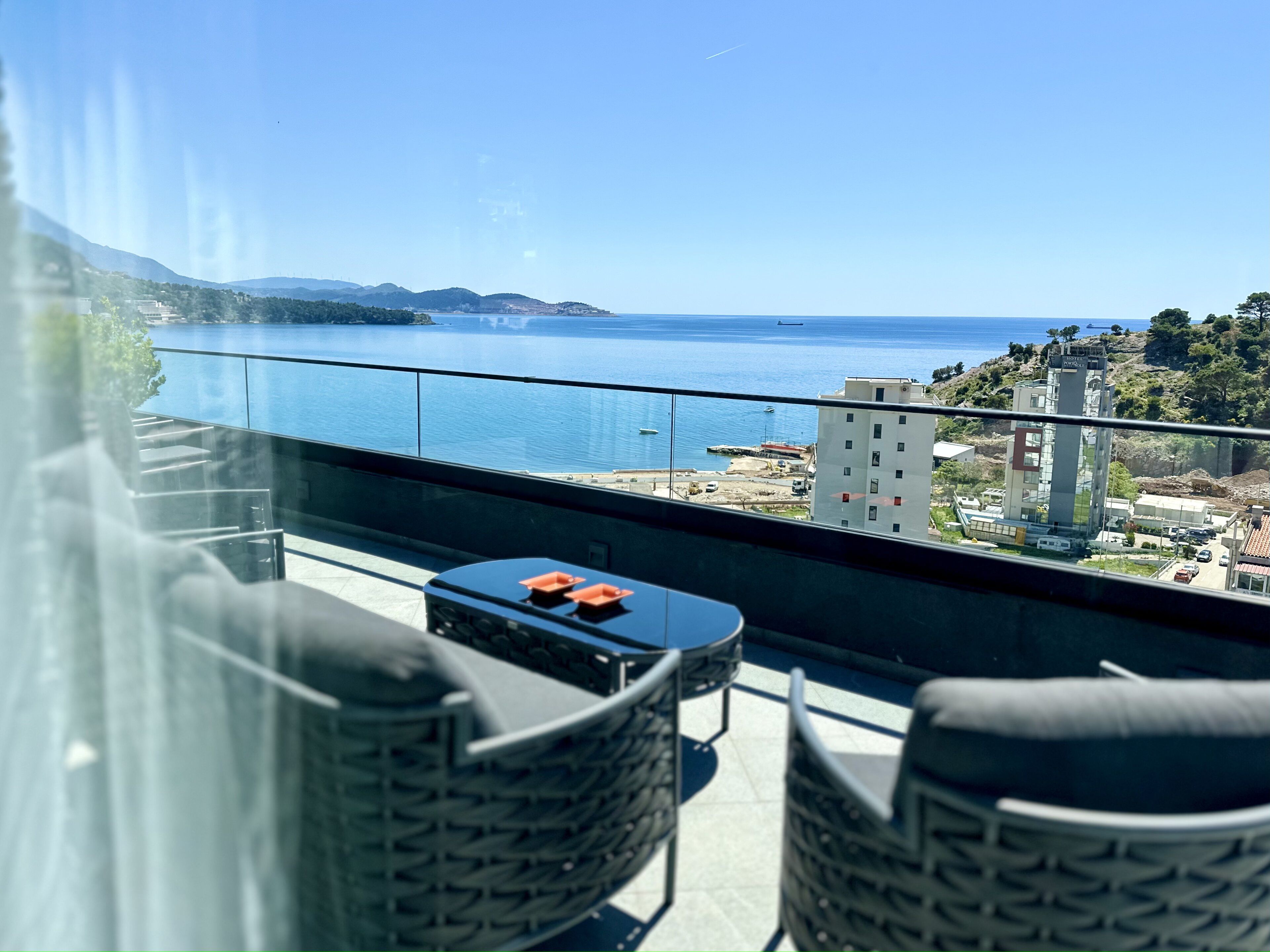 Un balcón con vistas al mar, una mesa con sillas y un edificio al fondo.