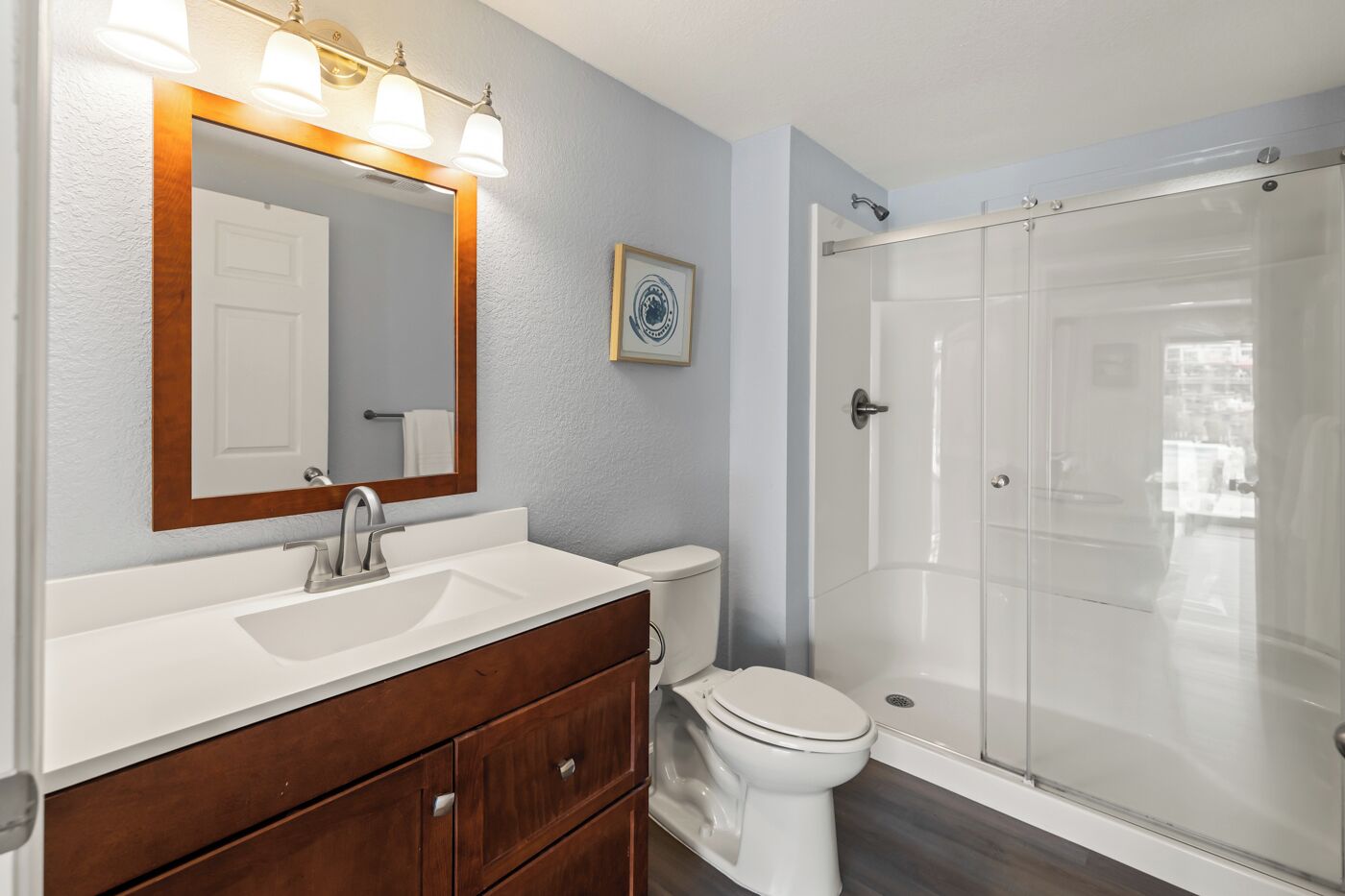 A bathroom with a white sink, wooden vanity, a toilet, and a glass-enclosed shower.