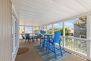 Une terrasse extérieure couverte, avec une table et des chaises, donnant sur les maisons voisines, et une porte située sur le côté gauche.