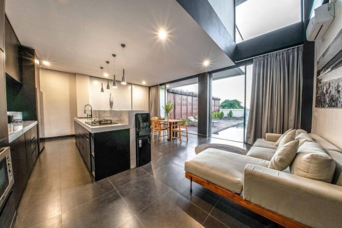 A modern kitchen with dark cabinetry, a dining area with a table and chairs, and a living area with a sofa.