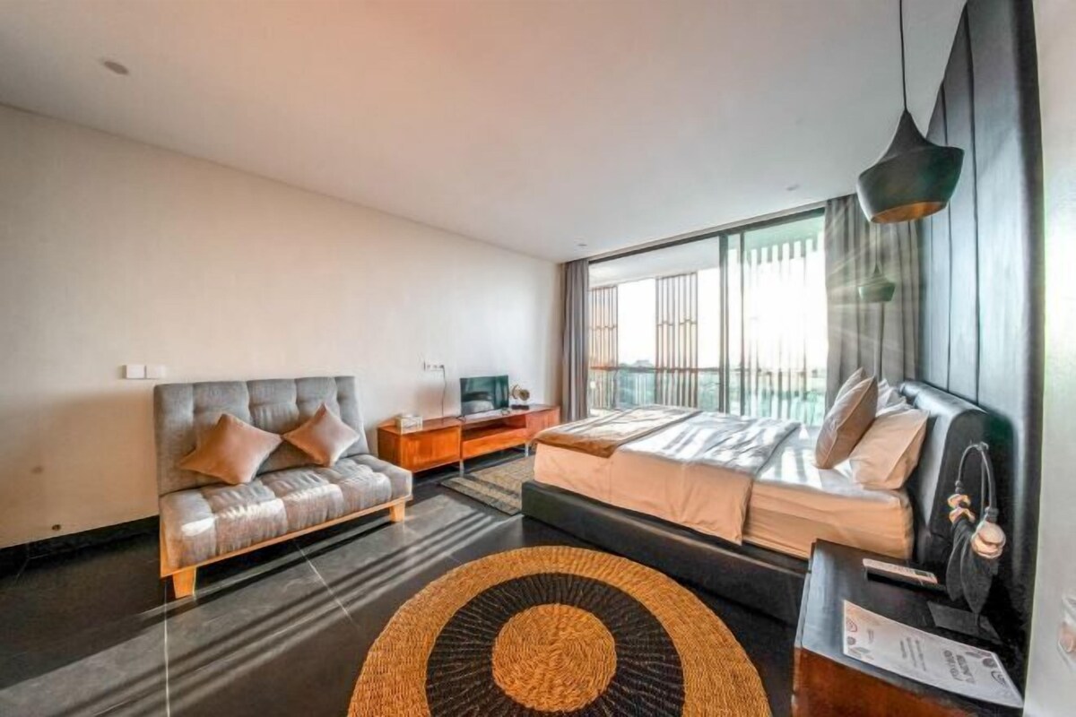 A modern hotel room with a bed, sofa, TV, and large windows.