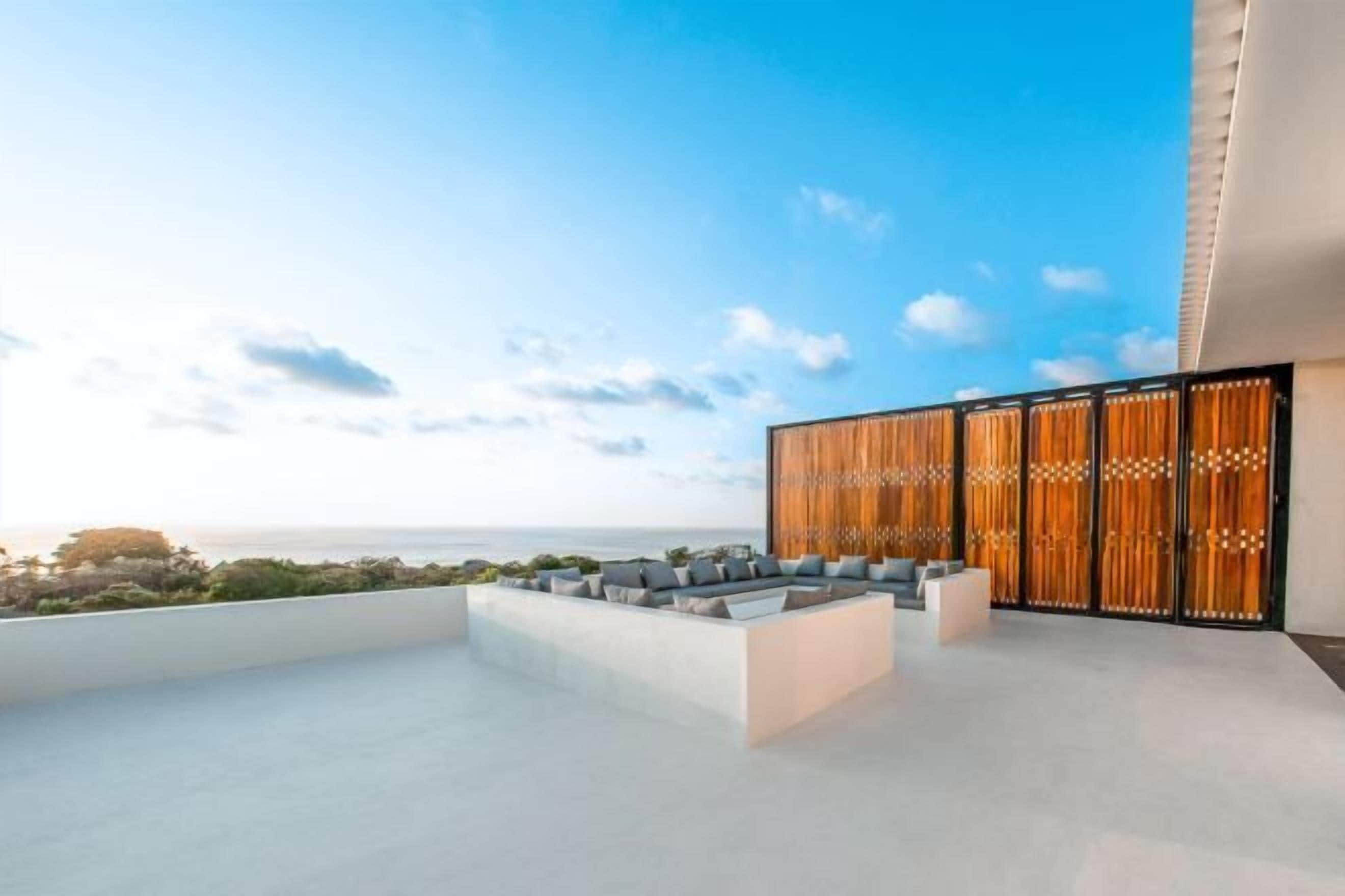 Eine Dachterrasse mit Sitzgelegenheit, einer Holzabtrennung und Blick auf das Meer.