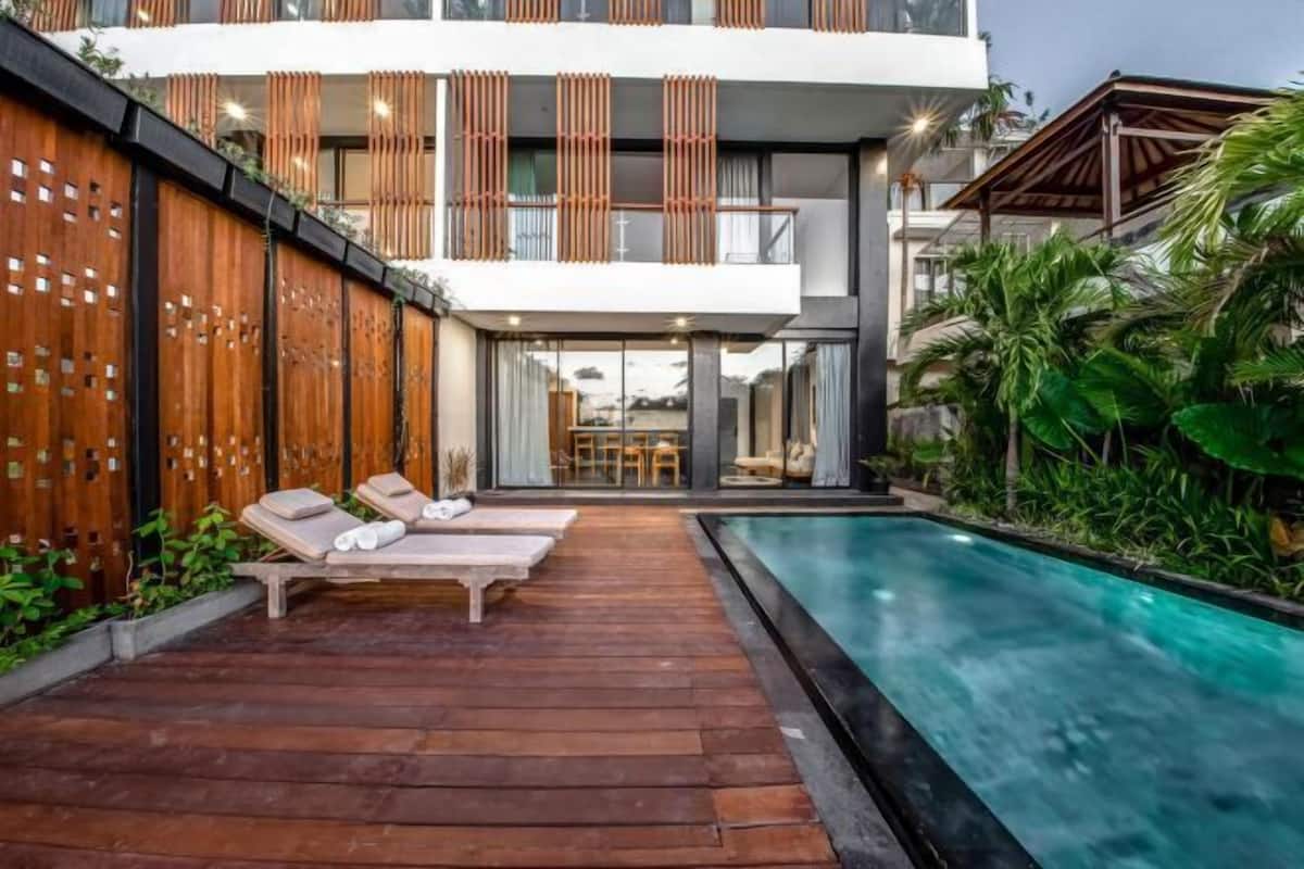 A modern house with a pool, wooden deck, and lounge chairs.
